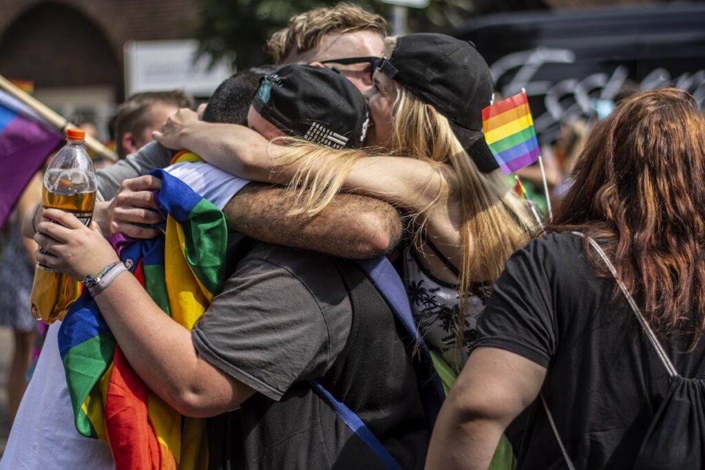 Priatelia sa objímajú na Pride, v rukách dúhové vlajky